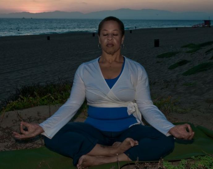 Black woman seated cross legged on beach at sunset